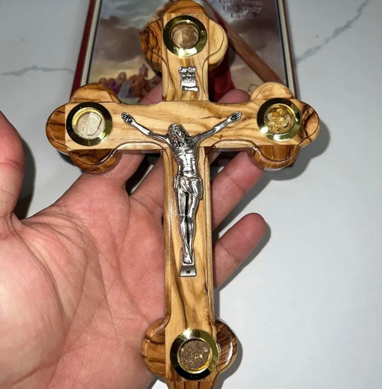 A small Olive Wood Budded Crucifix with Four Holy Elements hand-held over a Bible.