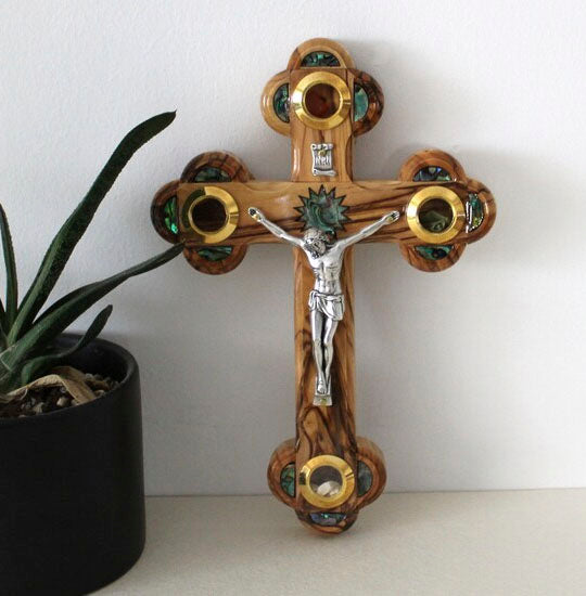 Olive Wood Budded Crucifix with Four Holy Elements leaning on a white wall.