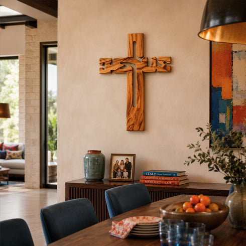 Wooden cross on a wall above a dining table with books and decor items.