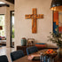 Wooden cross on a wall above a dining table with books and decor items.