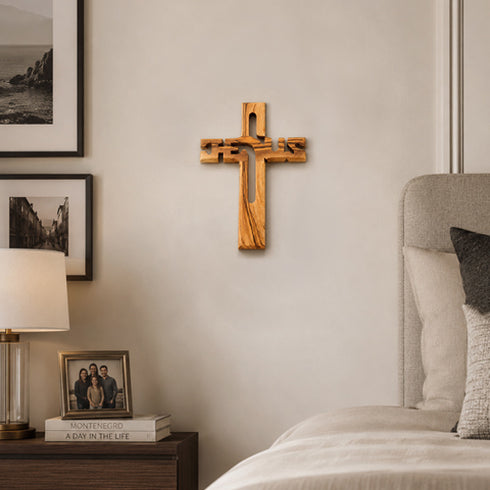 Wooden cross on a wall above a bed with decor items.