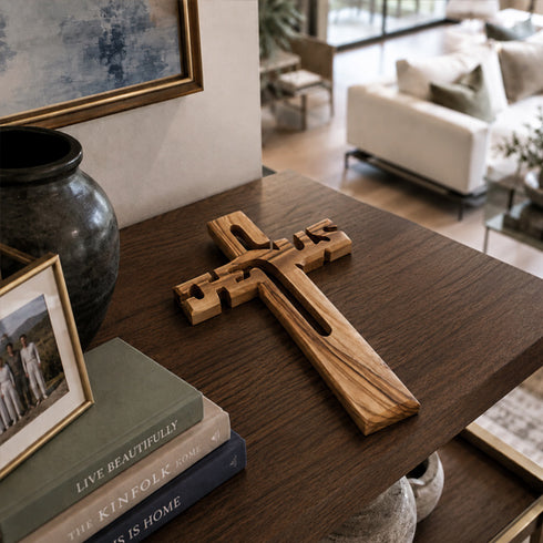 Wooden cross on a table with books and a vase in a living room setting