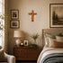 Nestled bedroom with a wooden cross, lamp, and framed pictures on a beige wall.