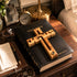 Black Holy Bible with a wooden cross on a wooden surface, surrounded by decorative items.