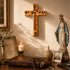 Wooden cross, statue of a religious figure, candle, and Bible on a wooden surface.