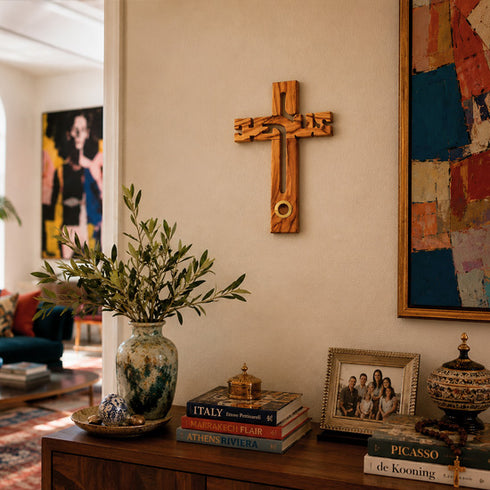 Wooden cross on a wall above a wooden cabinet with books, a vase, and a family photo.
