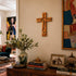 Wooden cross on a wall above a wooden cabinet with books, a vase, and a family photo.