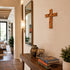 Wooden cross on a wall above a console table with books and a vase.