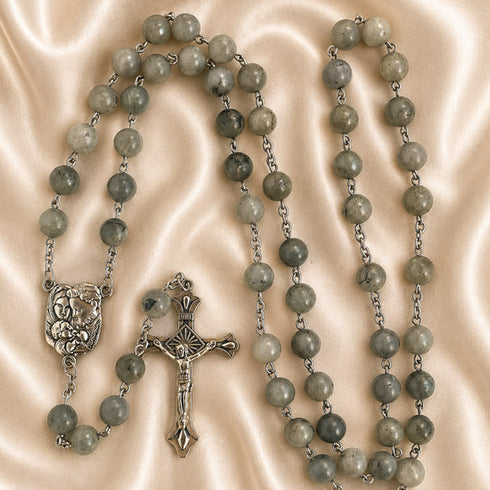 A rosary with green marbled beads, a crucifix and a small medallion, on a beige satin fabric background.