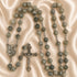 A rosary with green marbled beads, a crucifix and a small medallion, on a beige satin fabric background.