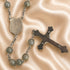 A rosary with round gray stone beads, a silver-tone centerpiece, and a metal crucifix, on a satin beige fabric background.