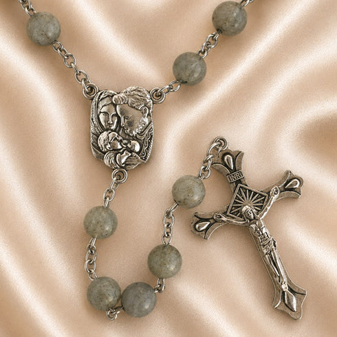 A rosary with gray round beads, a silver-tone medallion, and a crucifix, arranged on a satin fabric background.
