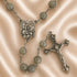 A rosary with gray round beads, a silver-tone medallion, and a crucifix, arranged on a satin fabric background.