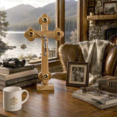Wooden crucifix on a table with books and a mug, window view of a lake and mountains.
