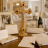 Wooden cross with Jesus figure on a table with wedding photos, champagne, and glasses.