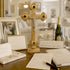 Wooden cross with Jesus figure on a table with wedding photos, champagne, and glasses.