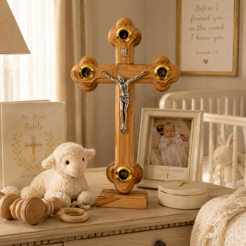 Wooden cross with Jesus figure on a shelf with toys and a baby photo in a nursery setting.