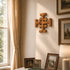 Wooden cross on a wall with framed family photos and a lamp in a room with a window and curtains.