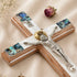 Decorative crucifix with wooden cross, silver Jesus figure, and abalone shell inlay on a beige fabric background.