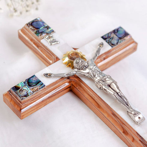 A standing Olive Wood Latin Crucifix with Mother of Pearl accents, silver Jesus figure, surrounded by flowers.
