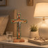Decorative cross on a nightstand with a lamp, glass, and book in the background.