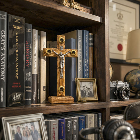 Wooden latin cross with Jesus corpus on a bookshelf with medical books and personal photos.