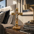 Wooden cross with gold accents on a nightstand next to a bed with pillows and a lamp.