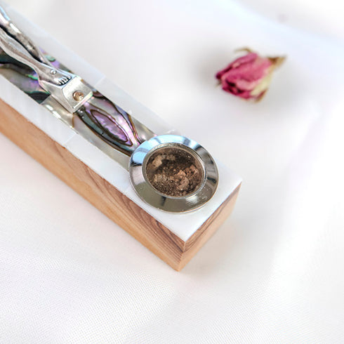 Zoomed image of a bottom of a latin-style olive wood cross with silver crucifix, decorated with green and white mother of pearl, and holy soil capsule, against a white background.