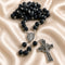 A black lava stone rosary with silver metal links, a round medallion, and a detailed crucifix pendant, on a satin background.