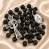 A black lava stone rosary with silver-tone metal links, a detailed crucifix, a round Miraculous Medal,on a beige fabric background.