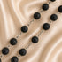 A strand of black lava stone beads connected by silver-toned metal chains, laid across draped satin fabric.