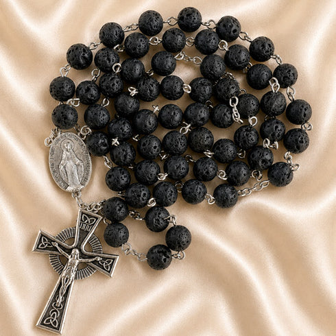 A black lava stone rosary with silver-tone metal links, a Miraculous Medal pendant, and a crucifix.
