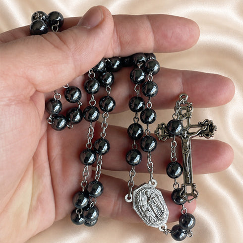 Hematite bead rosary held in hand, showing dark beads, oval medal, and metal crucifix