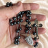 Hematite bead rosary held in hand, showing dark beads, oval medal, and metal crucifix
