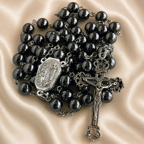 Hematite bead rosary laid flat with oval devotional medal and ornate crucifix