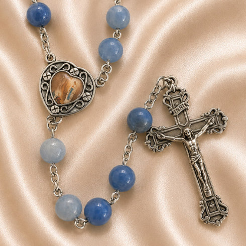 A rosary with blue beads, a silver centerpiece, and an ornate silver crucifix, on a satin beige fabric background.