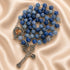 A blue stone rosary rosary with a silver-toned crucifix and heart-shaped medallion, on a beige satin fabric background.
