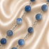 A beaded necklace featuring blue gemstone beads linked by silver-toned metal chains, on a beige fabric background.