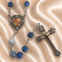 A rosary with blue beads, a silver-tone centerpiece medallion, and an ornate silver-tone crucifix, on a beige satin background.
