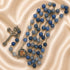 A rosary necklace with blue beads, a silver-tone crucifix, and a heart medallion, on a beige satin fabric background.