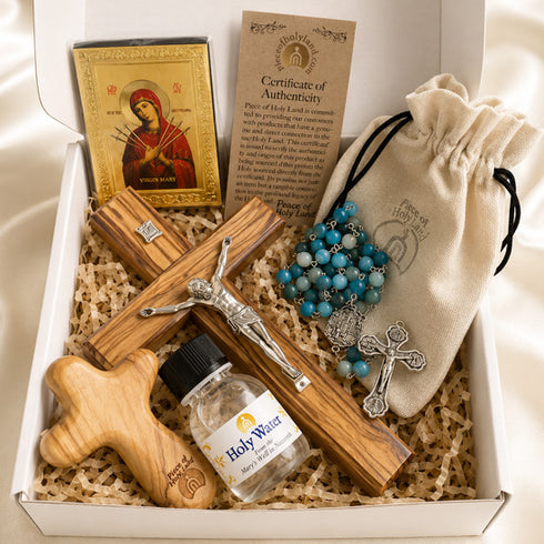 A religious gift set in a white box with a wooden cross, a bottle of holy water, a blue beaded rosary and a certificate