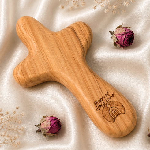 Wooden comfort cross with 'Piece of Holy Land' branding on a soft fabric background with dried flowers.