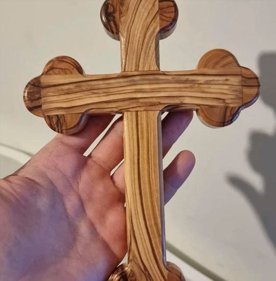Large orthodox budded olive wood cross hand held against a white wall.