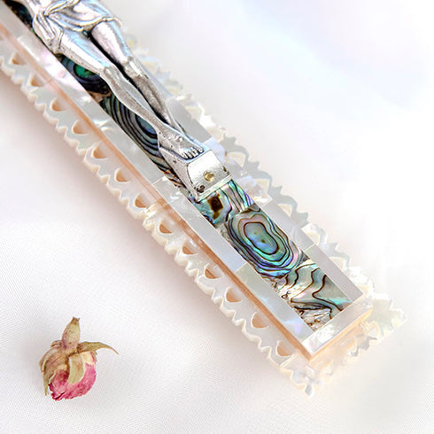 Zoomed image of a bottom of a latin-style olive wood cross with silver crucifix, decorated with mother of pearl, against a white background.