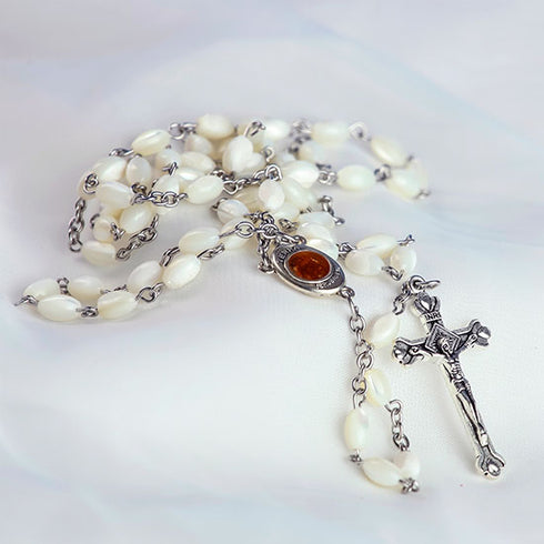 Packshot of a handmade Mother of Pearl rosary with Holy Soil centrepiece featuring a an iron crucifix, laid on white cloth.