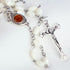 Close up of a handmade Mother of Pearl rosary with Holy Soil centrepiece featuring a an iron crucifix, laid on white cloth.