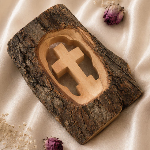 Wooden cross carved into a wooden block with natural wood texture on a soft fabric background.