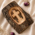 Wooden cross carved into a wooden block with natural wood texture on a soft fabric background.