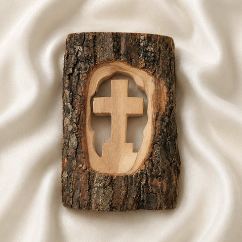 Wooden cross carved into a piece of tree bark on a white fabric background
