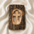 Wooden cross carved into a piece of tree bark on a white fabric background